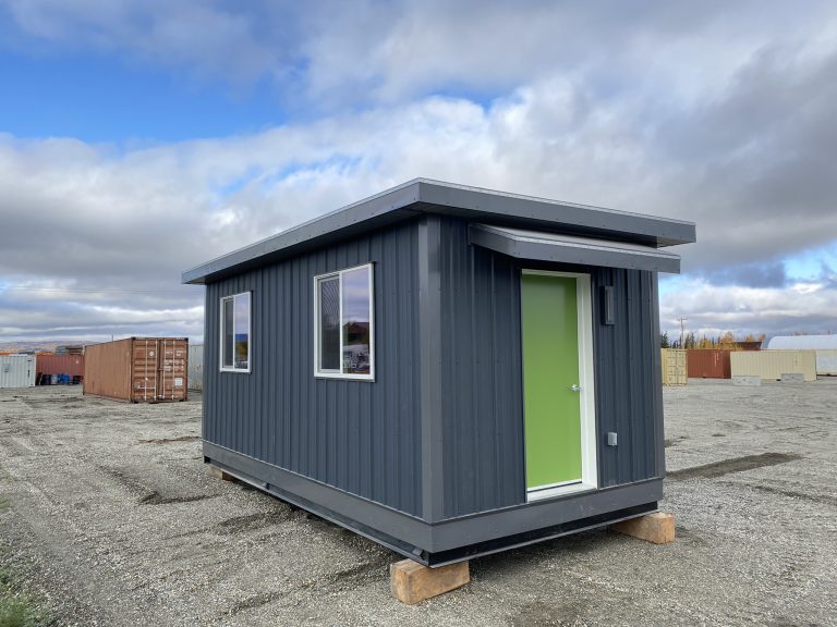 Modular office building with metal siding and a green entry door set on a gravel lot, representing portable workspace solutions for job sites