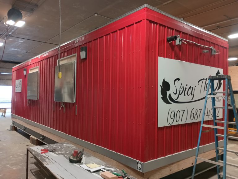 Custom modular food service building under construction in Alaska, featuring a red exterior, service window, and signage for a mobile kitchen or concession use